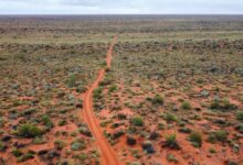 Explore the vast and rugged Australian Outback with this stunning aerial view showcasing a remote dirt road stretching t