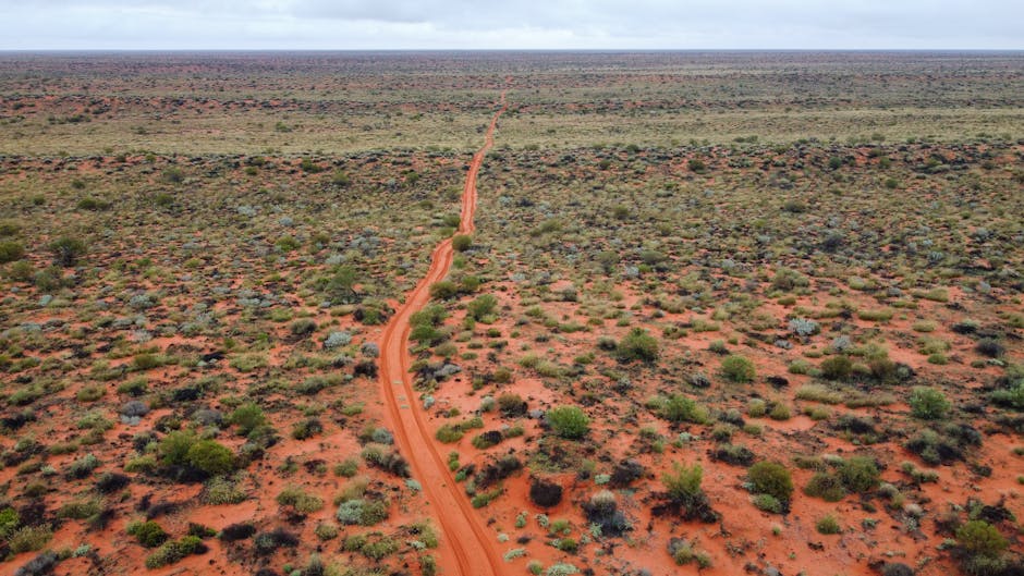 Explore the vast and rugged Australian Outback with this stunning aerial view showcasing a remote dirt road stretching t