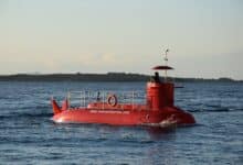 A bright red semi-submarine cruising on a calm ocean with a distant shoreline.