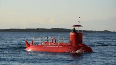 A bright red semi-submarine cruising on a calm ocean with a distant shoreline.