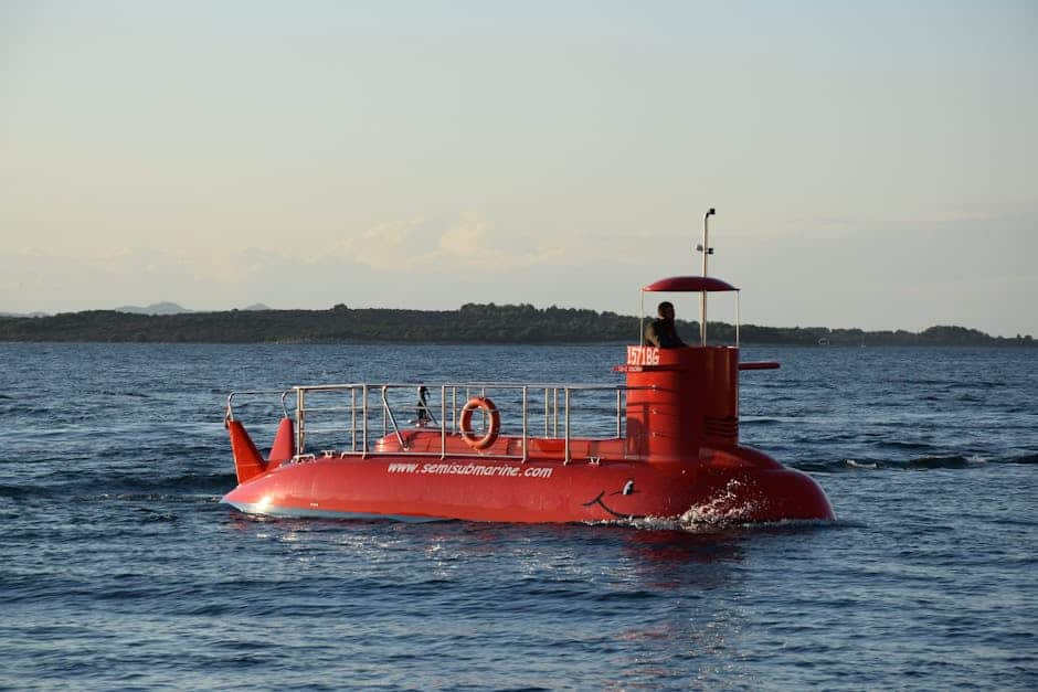 A bright red semi-submarine cruising on a calm ocean with a distant shoreline.
