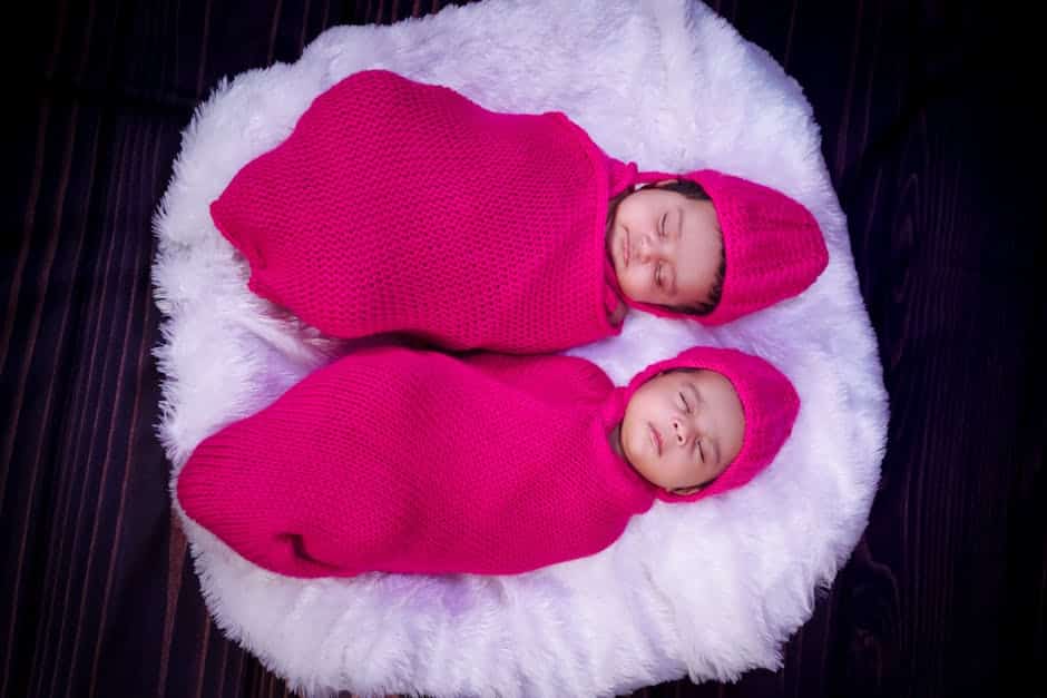 Charming image of twin babies peacefully sleeping in pink knit swaddles on a fluffy surface.