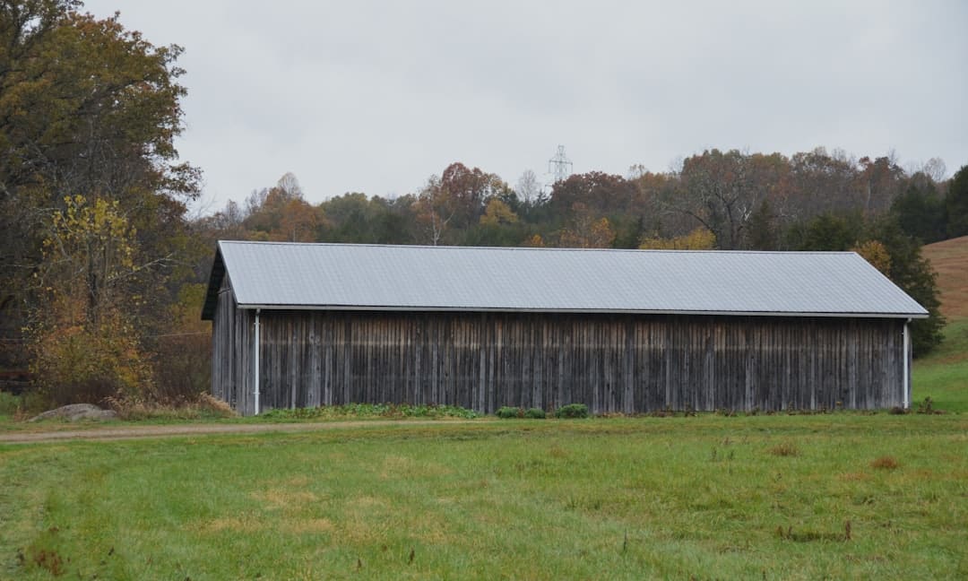 Long wooden barn with metal roof in field.