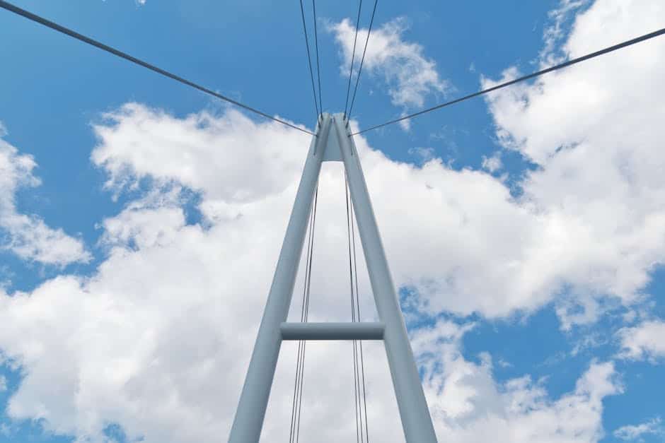 Upward view of a modern cable-stayed bridge with a blue sky and clouds backdrop.