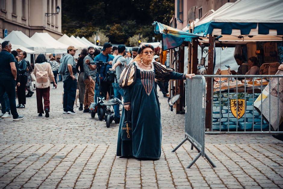 A bustling renaissance fair with a woman in period dress among the visitors and market stalls.